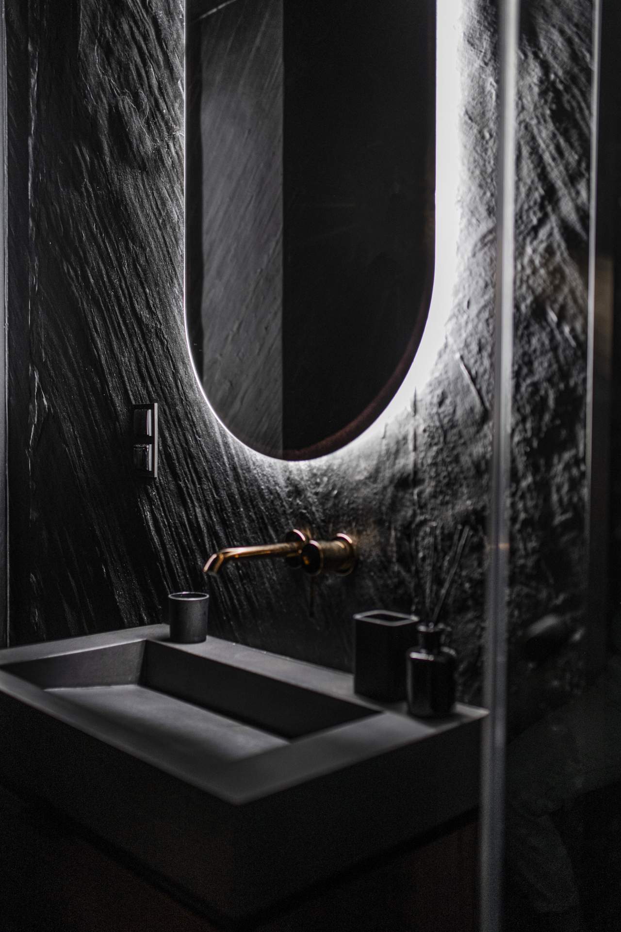 Masowa Stone - Stone Veneer Experts in Scotland. Modern dark bathroom sink with a wall-mounted faucet and an illuminated oval mirror on textured wall.