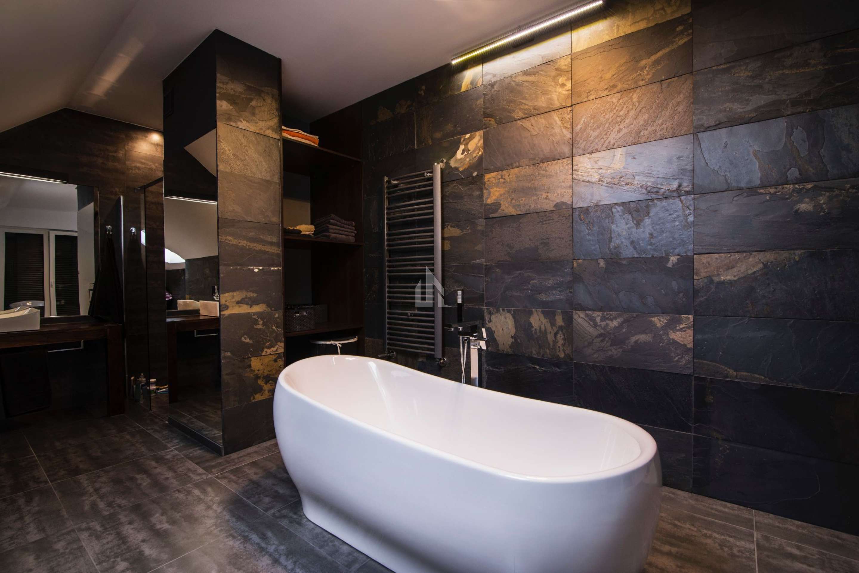 Masowa Stone - Stone Veneer Experts in Scotland. Modern bathroom with a freestanding white bathtub, dark stone tiled walls and floor, and shelves with folded towels.