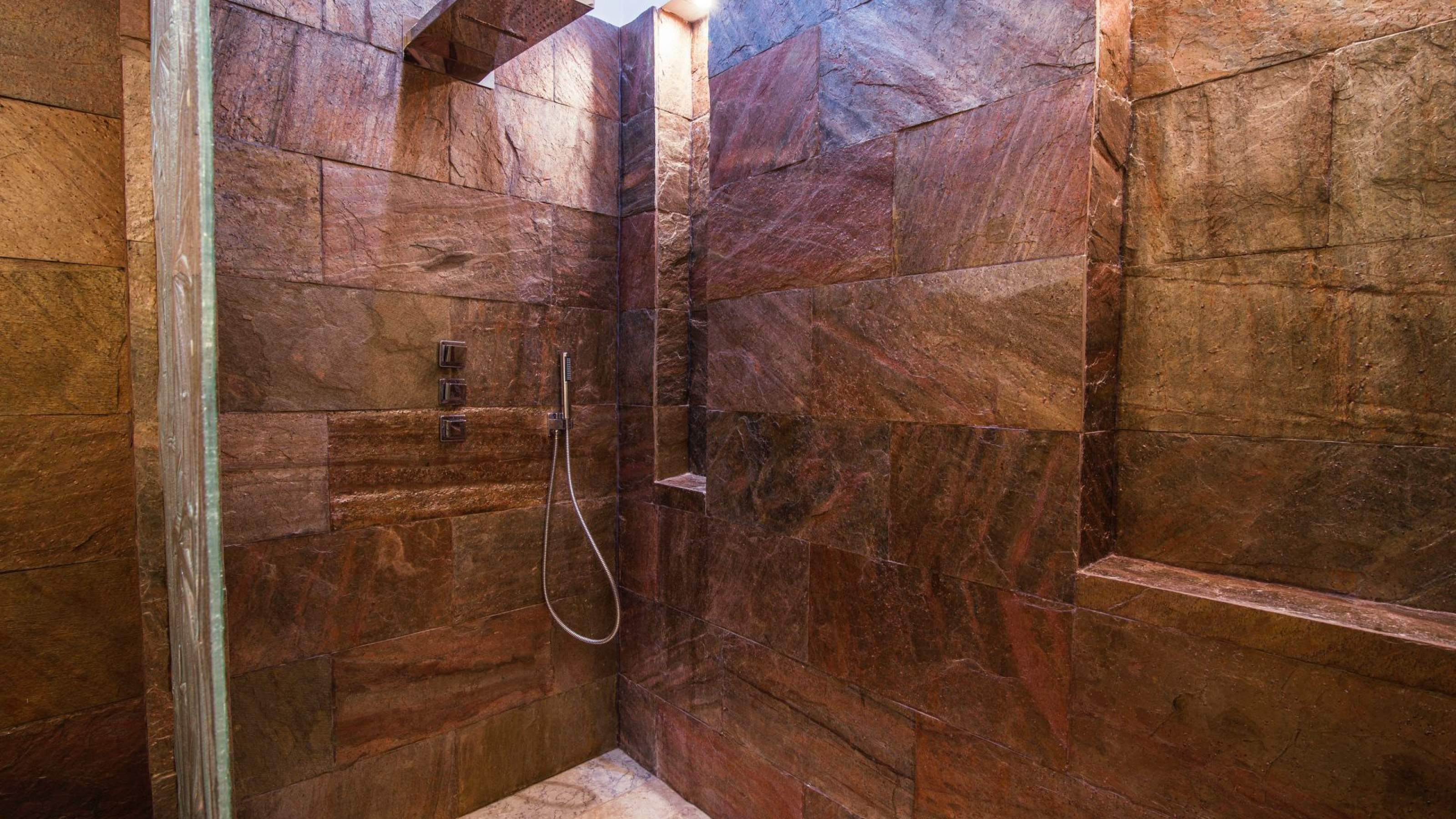 Masowa Stone - Stone Veneer Experts in Scotland. Modern shower area with dark stone tiles, built-in niches, and a handheld showerhead attached to the wall.