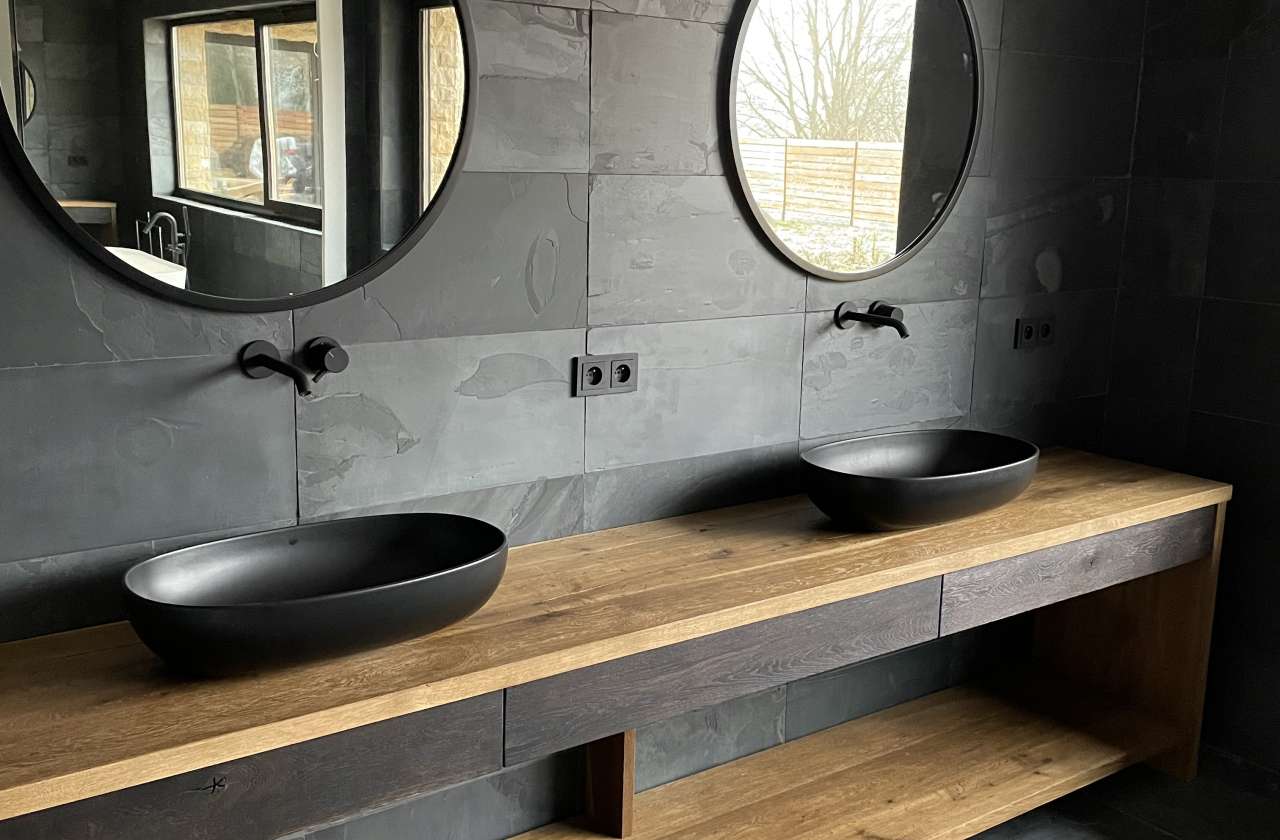 Masowa Stone - Stone Veneer Experts in Scotland. Modern bathroom with two black oval sinks on a wooden countertop and round mirrors above each sink.